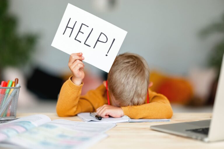 unhappy tired child boy student holds a sign HELP while doing homework at home