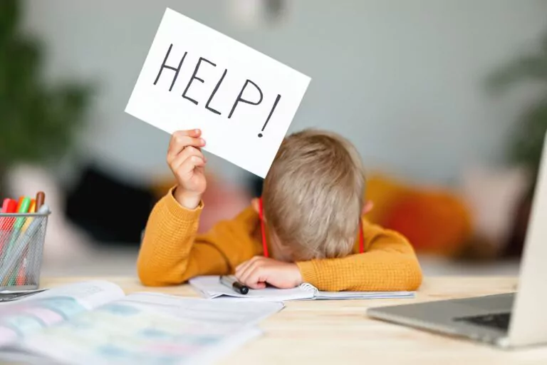 unhappy tired child boy student holds a sign HELP while doing homework at home